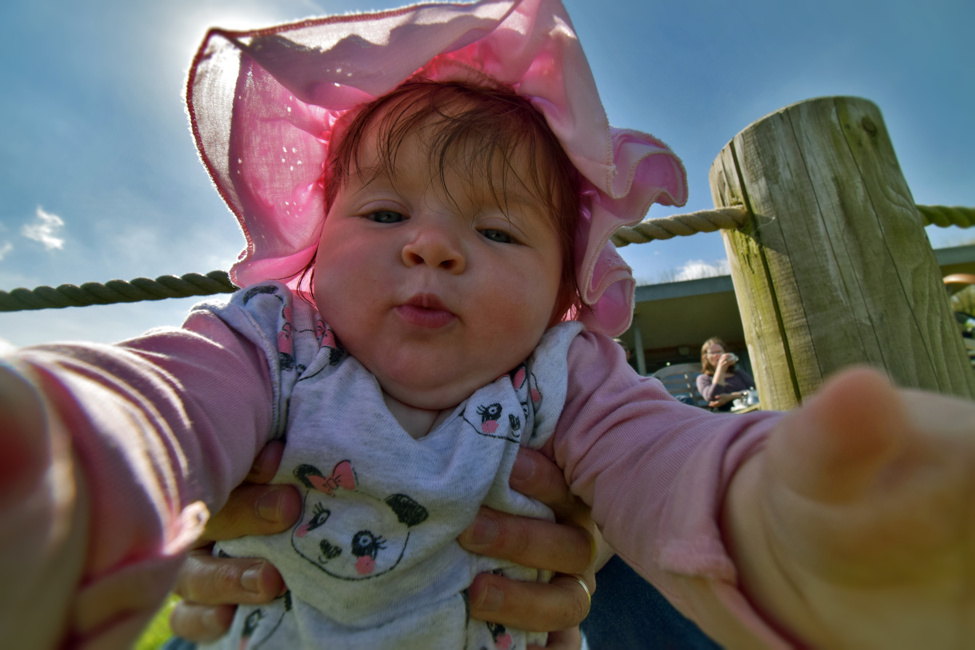 Lying down in the grass, I photograph a baby girl with a pink sun hat as she grabs the lens of my camera.